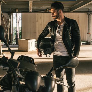 Man in leather jacket holding motorcycle helmet.