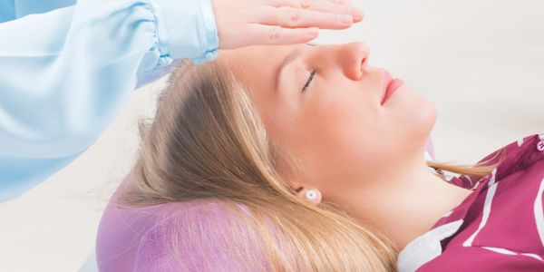 A woman receiving a calming energy healing session with hands above her head.