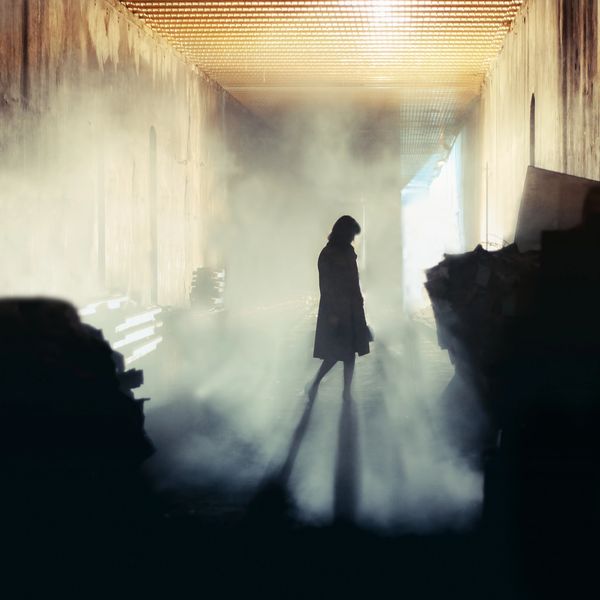 Silhouette of a person standing in a foggy, dimly lit corridor with long shadows.