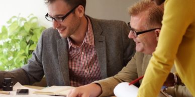 Three colleagues collaborating and smiling over documents at a desk.