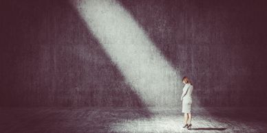 Woman standing alone in a spotlight in a dark, empty room.