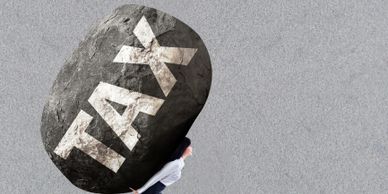 A woman struggling to carry a huge rock labeled 'TAX'.