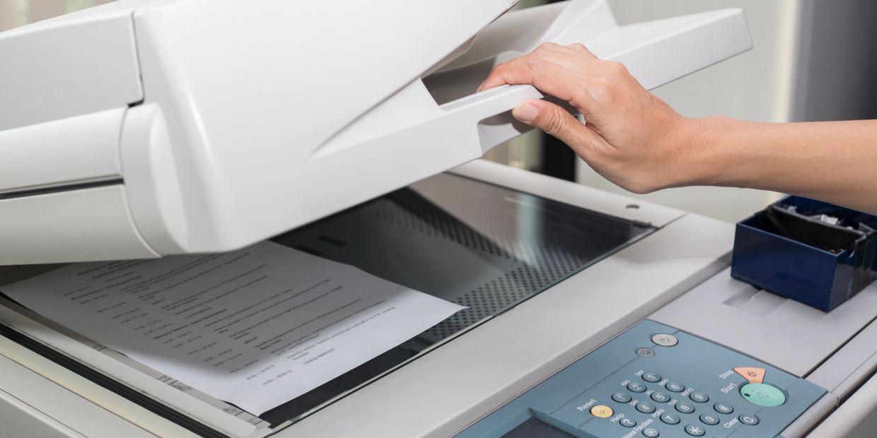 Hand lifting the lid of a copier with a document inside.