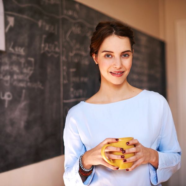 A teacher holding a hot drink of tea or coffee in front of a blackboard