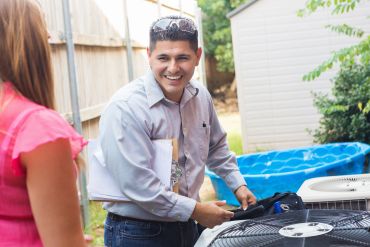 Technician smiling while inspecting an air conditioner outdoors.
