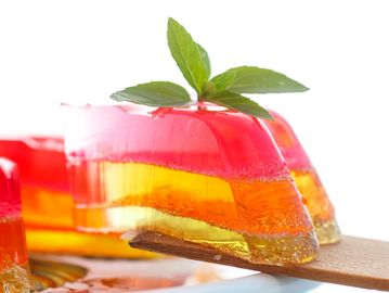 Colorful layered gelatin dessert garnished with mint leaves on a wooden spatula.