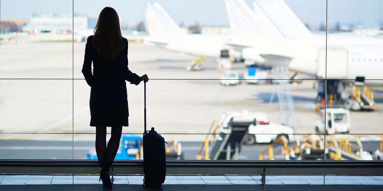 Woman with suitcase looking out at planes from airport terminal.