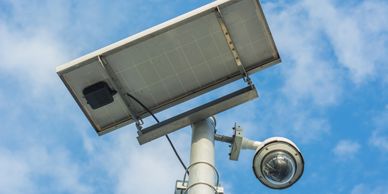 Solar-powered security camera mounted on a pole against a blue sky.