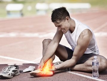 Athlete sitting on track holding his painful glowing ankle injury.