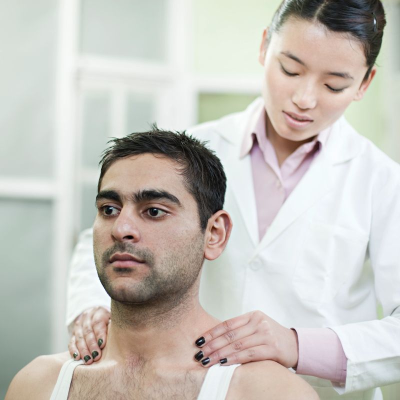 Indoor shoot at hospital in rehabilitation department. Female occupational therapist/physiotherapist giving therapy to a male patient she is relieving Trapezius spasm of the patient. Two people, waist up, square composition with selective focus and copy space.