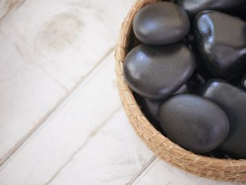 Smooth black stones in a woven basket on a white wooden surface.
