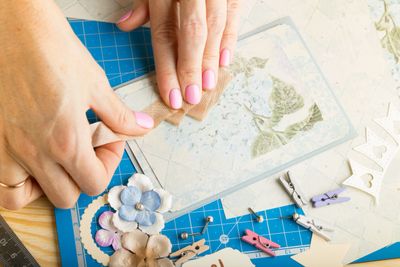 Hands peeling a stencil for crafting with decorative flowers and tools nearby.