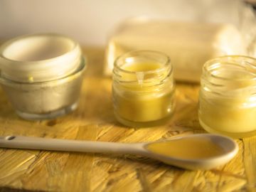 Jars of cream with a spoon on a wooden surface.
