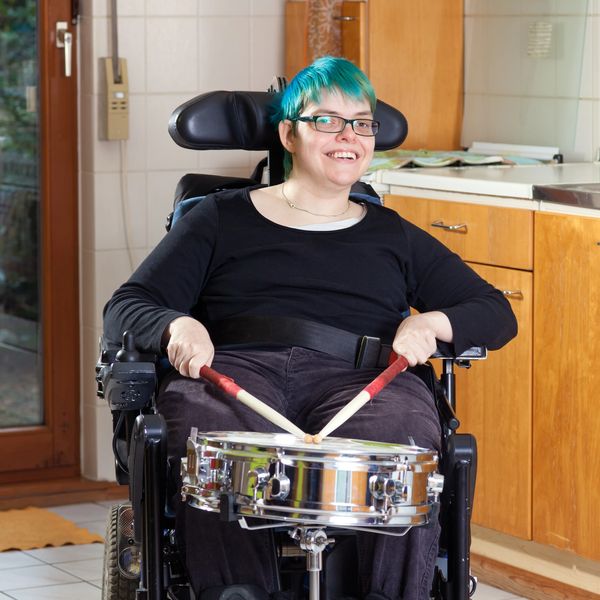 Person with teal hair playing a snare drum from a wheelchair.