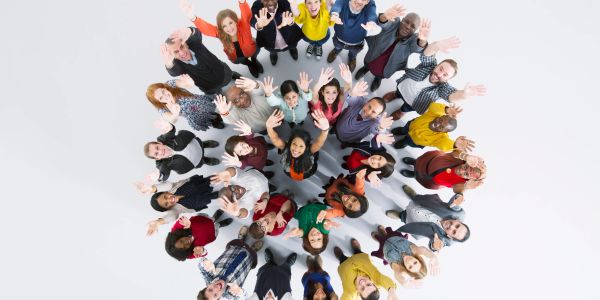 Diverse group of people standing in a circle, waving up at the camera.
