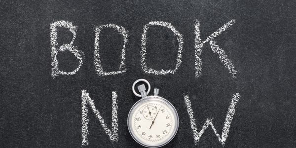 Chalkboard with 'BOOK NOW' and a stopwatch placed on it.