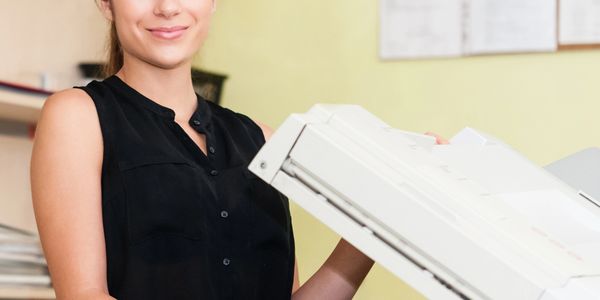 Smiling woman using a photocopier in an office setting.