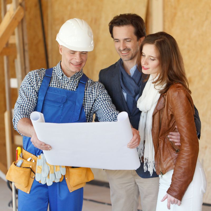 Worker shows house design plans to a young couple at construction site