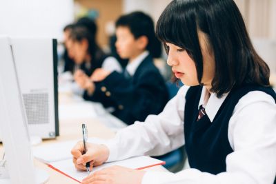 Student writing in a classroom with computers.