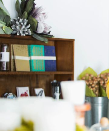 Books and floral decorations on a wooden shelf against a white wall.