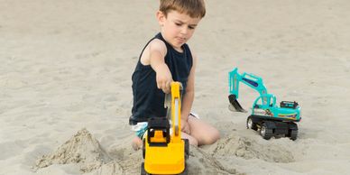 A boy playing with toy excavators in the sand.