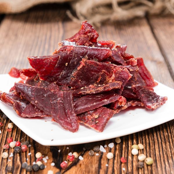 A plate of beef jerky on a wooden table with peppercorns and salt.