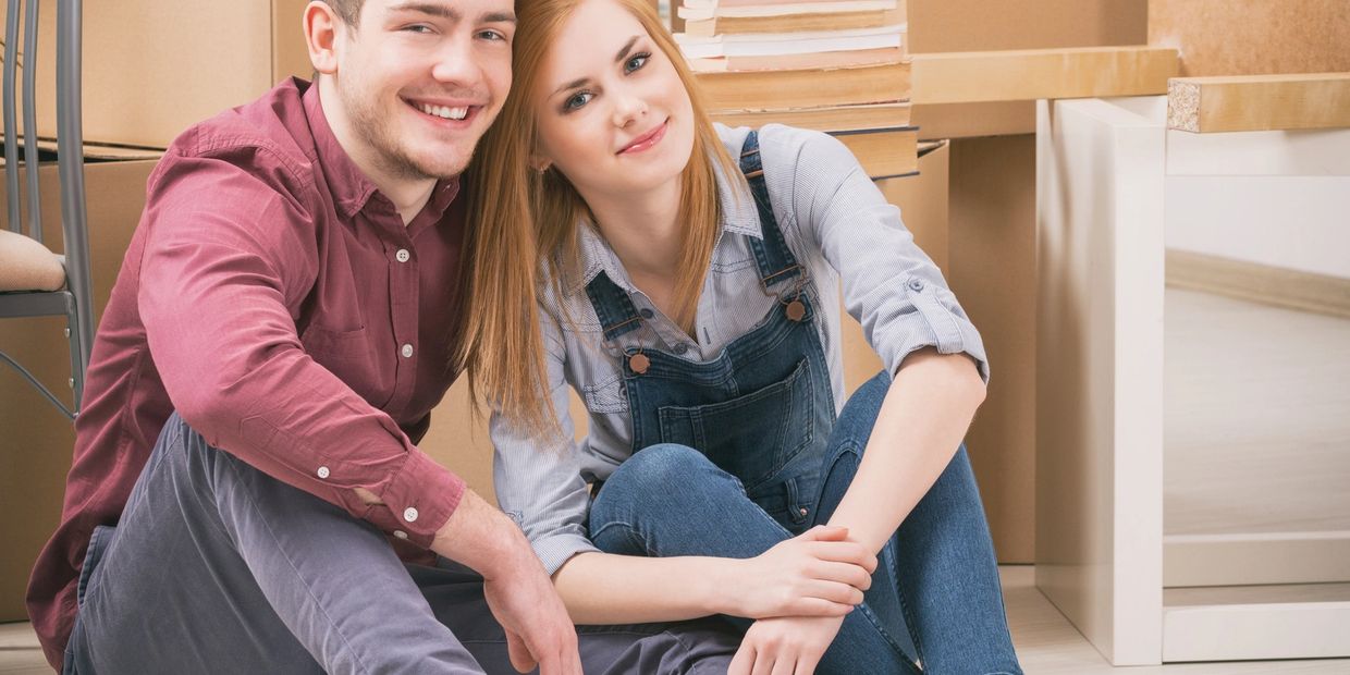 Happy couple sitting on the floor surrounded by moving boxes.