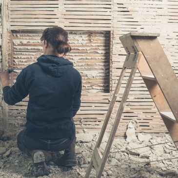 Person renovating wall beside a ladder.