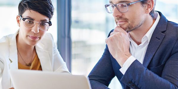 Two professionals analyzing information on a laptop in a modern office.