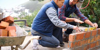 Two men building a brick wall, using a level for precision.