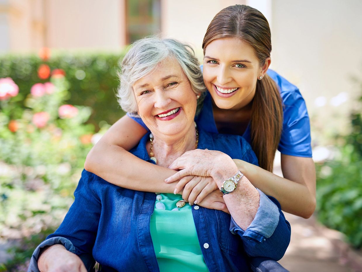 Young woman hugging elderly woman in a garden, both smiling happily.