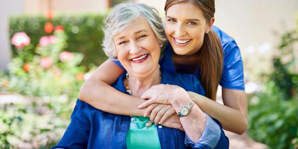 Young woman hugs elderly woman happily outdoors.