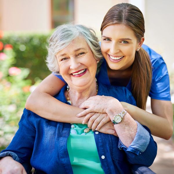 Young woman hugging elderly woman outdoors, both smiling.