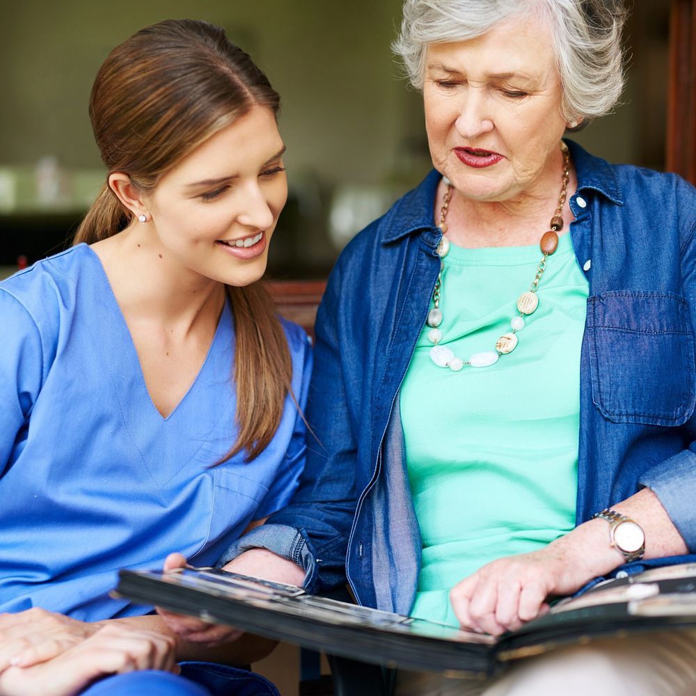 Young caregiver and elderly woman looking at a photo album together.