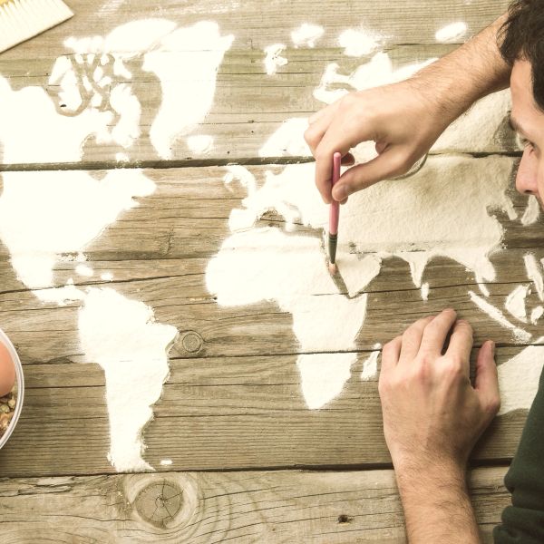Person painting a world map on wooden planks using white paint.