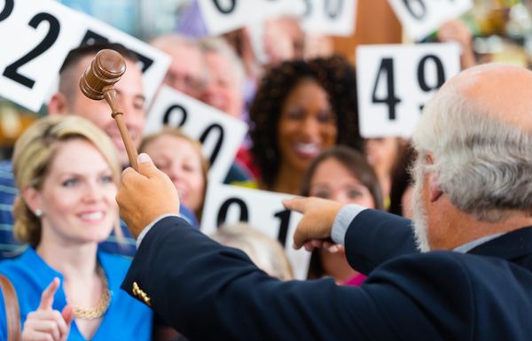 Auctioneer conducting a lively auction with bidders raising numbered paddles.