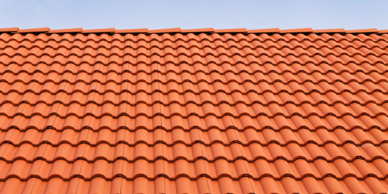 A close-up of an orange tiled roof under a clear blue sky.