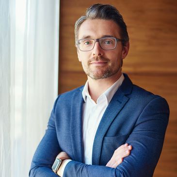 intelligent consulting lawyer with glasses wearing a suit but no tie, with his arms crossed