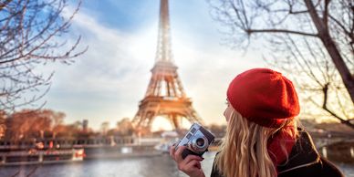 Woman in red beret holding camera near Eiffel Tower at sunset.