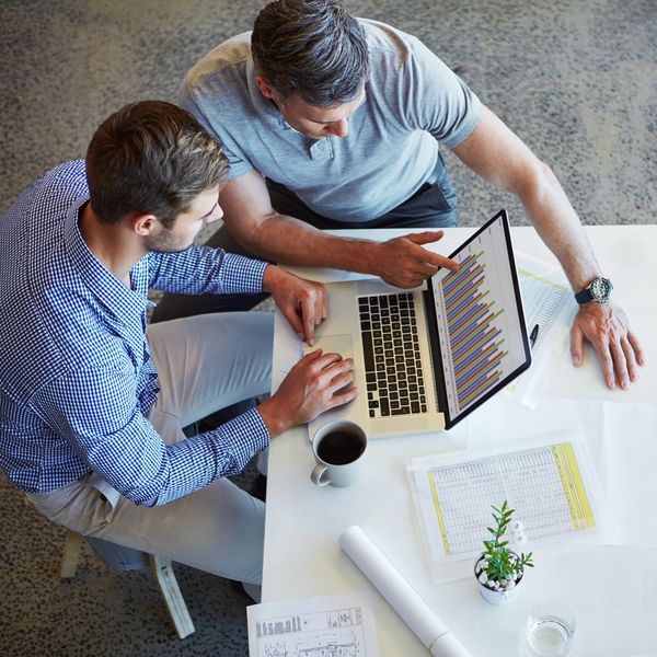 Two men analyzing colorful bar charts on a laptop during a meeting.