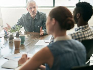 A man explaining something in a business meeting with colleagues.