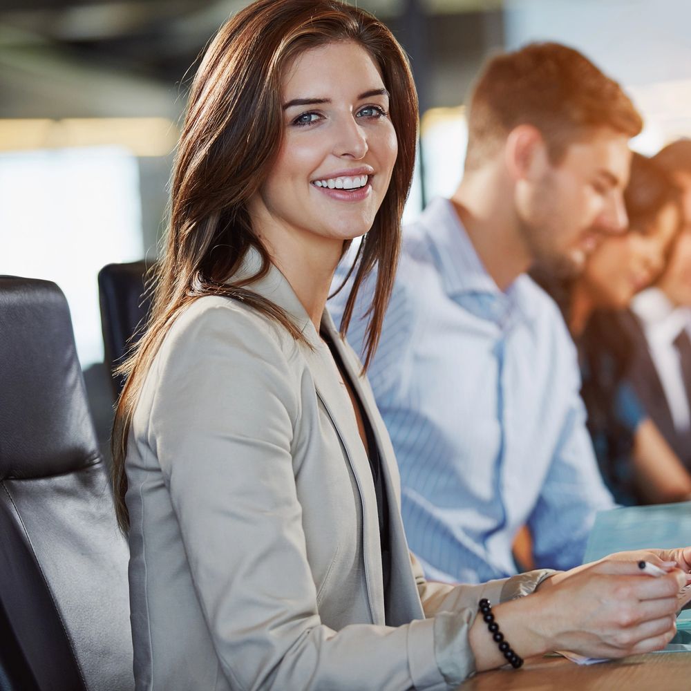 Smiling businesswoman in a meeting with colleagues in the background.