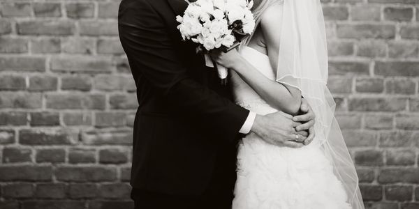 Black and white photo of a bride and groom embracing with a bouquet.