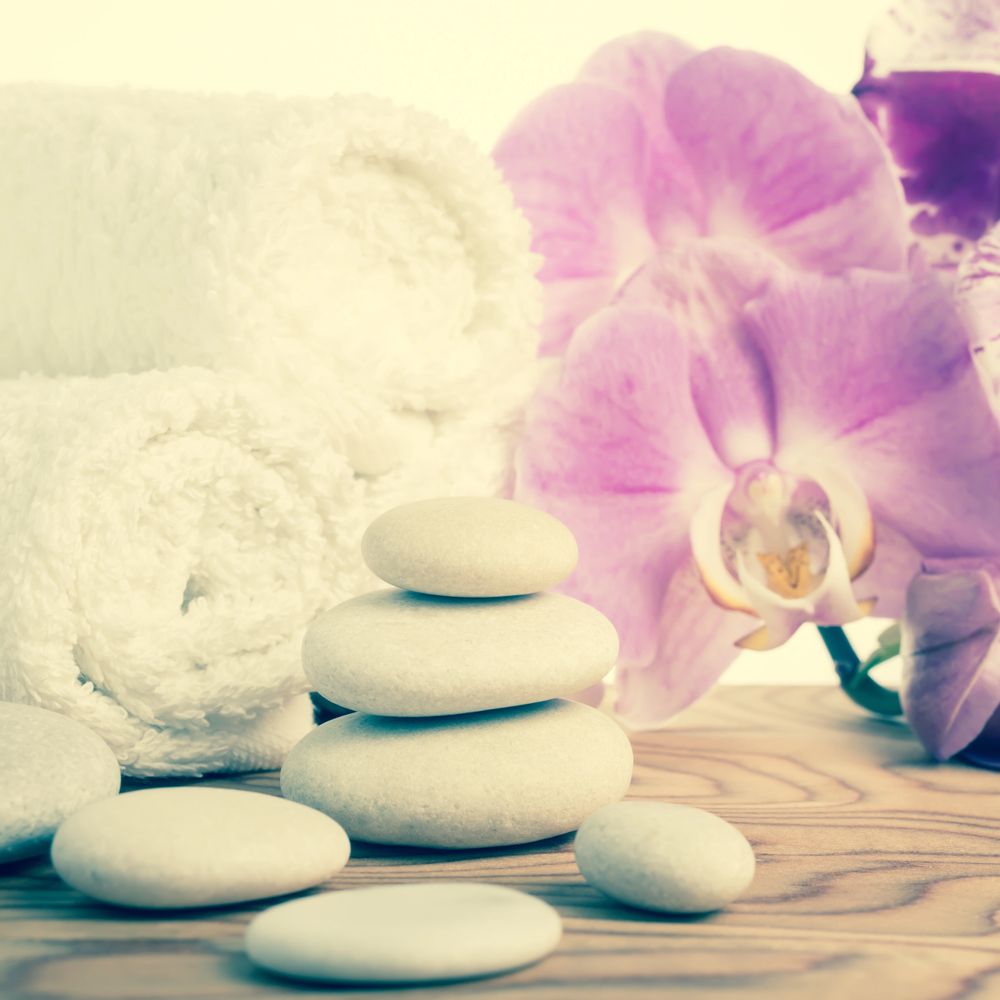 Stacked white spa stones with rolled towels and pink orchids on wooden surface.