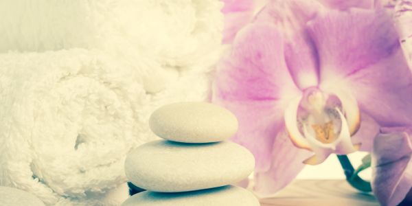 Stacked white spa stones with a white towel and pink orchid in the background.