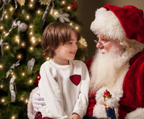 A child happily talks to Santa Claus near a Christmas tree.