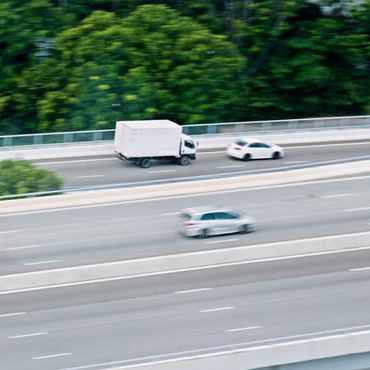 Vehicles speeding on a highway with greenery in the background.