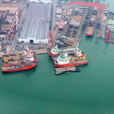 Aerial view of a busy shipyard with multiple docked vessels and industrial buildings.