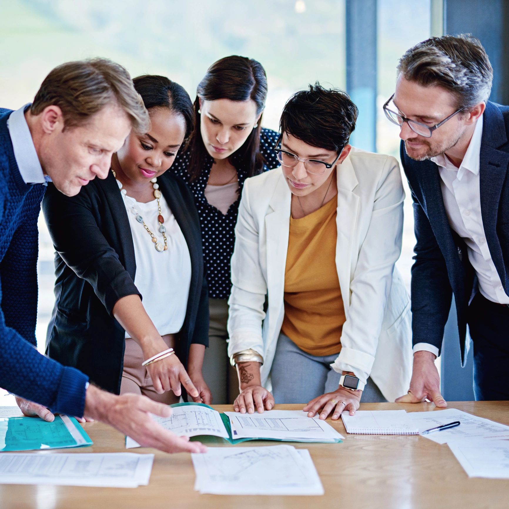 A diverse team collaborates over documents in a bright office.