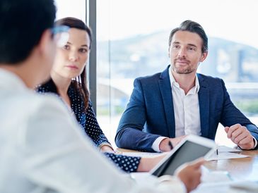 Three professionals engaged in a business meeting around a table with a tablet.